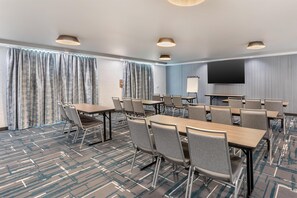 Une salle de conférence équipée d’une longue table, de chaises, d’un écran de projection et d’un grand téléviseur.