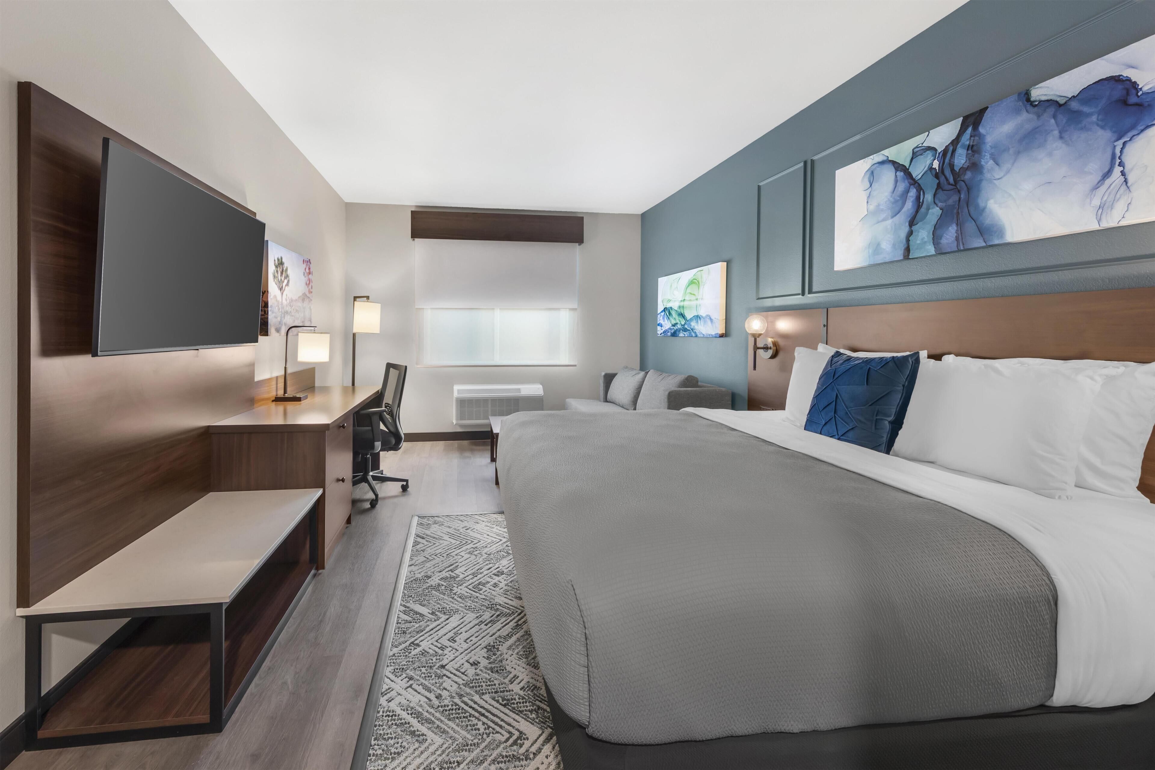 Una habitación de hotel moderna con una cama grande, un escritorio con una silla, un televisor de pantalla plana en la pared y obras de arte decorando las paredes.