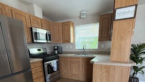 Een moderne keuken met houten kastjes, roestvrijstalen apparatuur en een raam met jaloezieën.