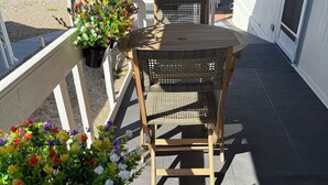 Een houten terras met een tafel en stoelen, omgeven door potplanten en een witte balustrade.