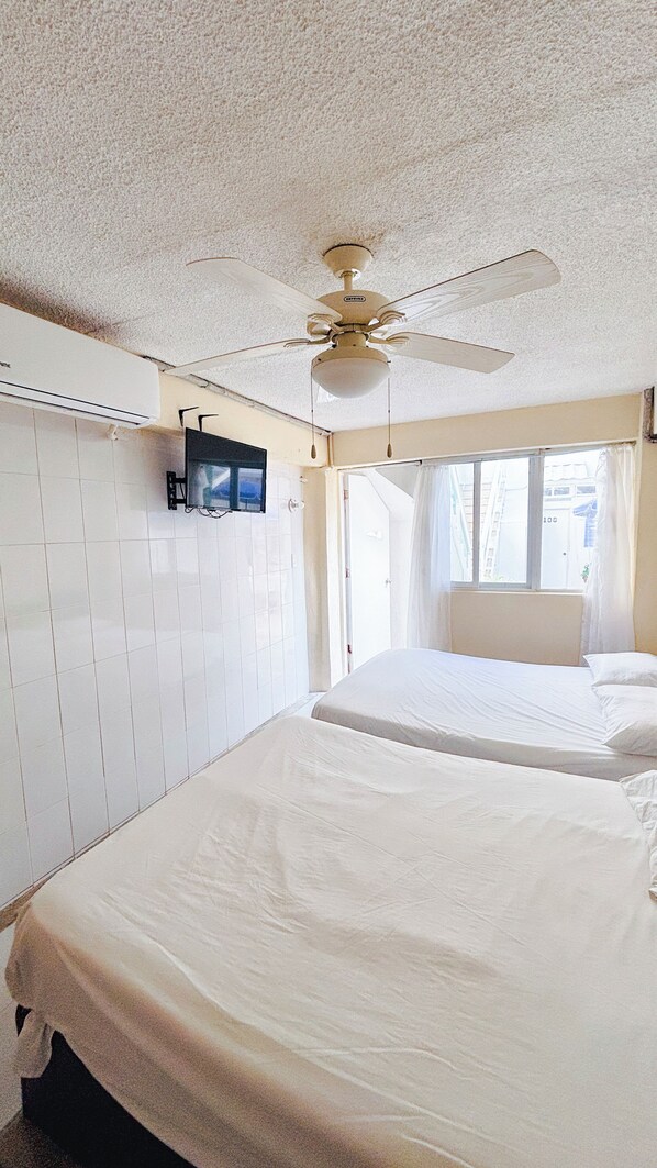 A hotel room with a ceiling fan, a TV mounted on the wall, and a bed with a canopy.