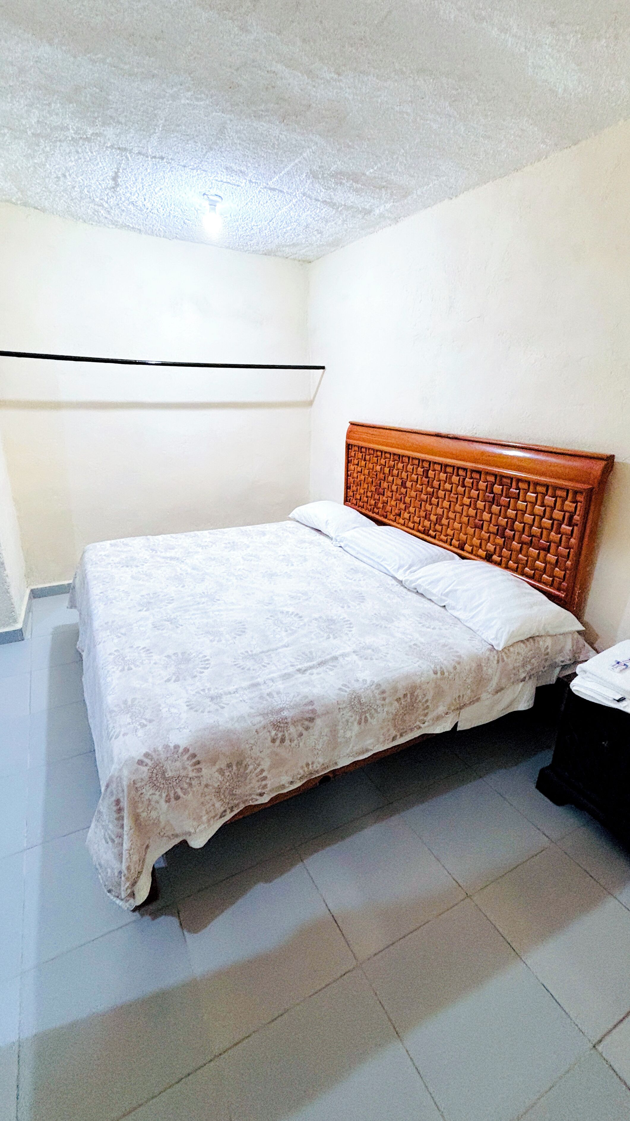 Un dormitorio con cabecera de madera, una cama con cubrecama blanco y una mesita de noche.