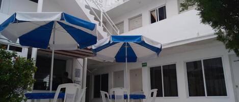 A building with a white exterior, a staircase, and outdoor seating with blue and white umbrellas.
