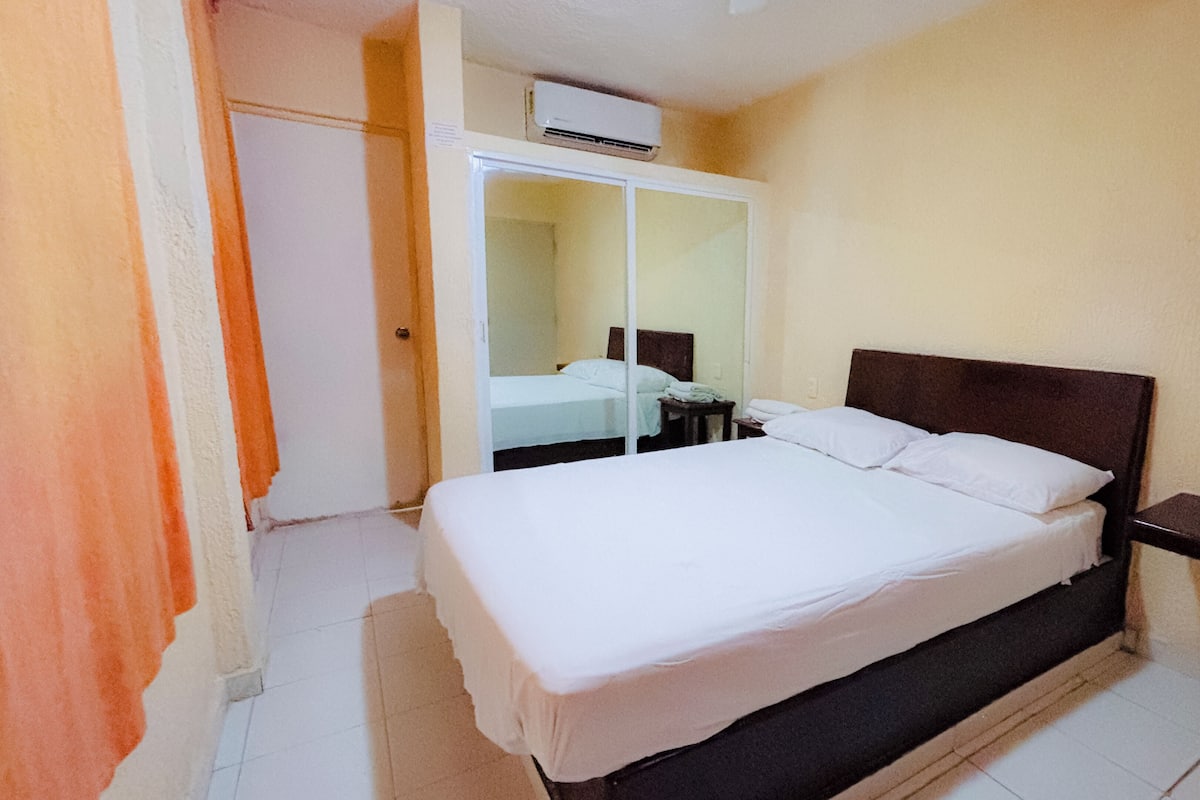 Ein Hotelzimmer mit einem großen Bett, einem Nachttisch, einem Kleiderschrank und einer Klimaanlage.