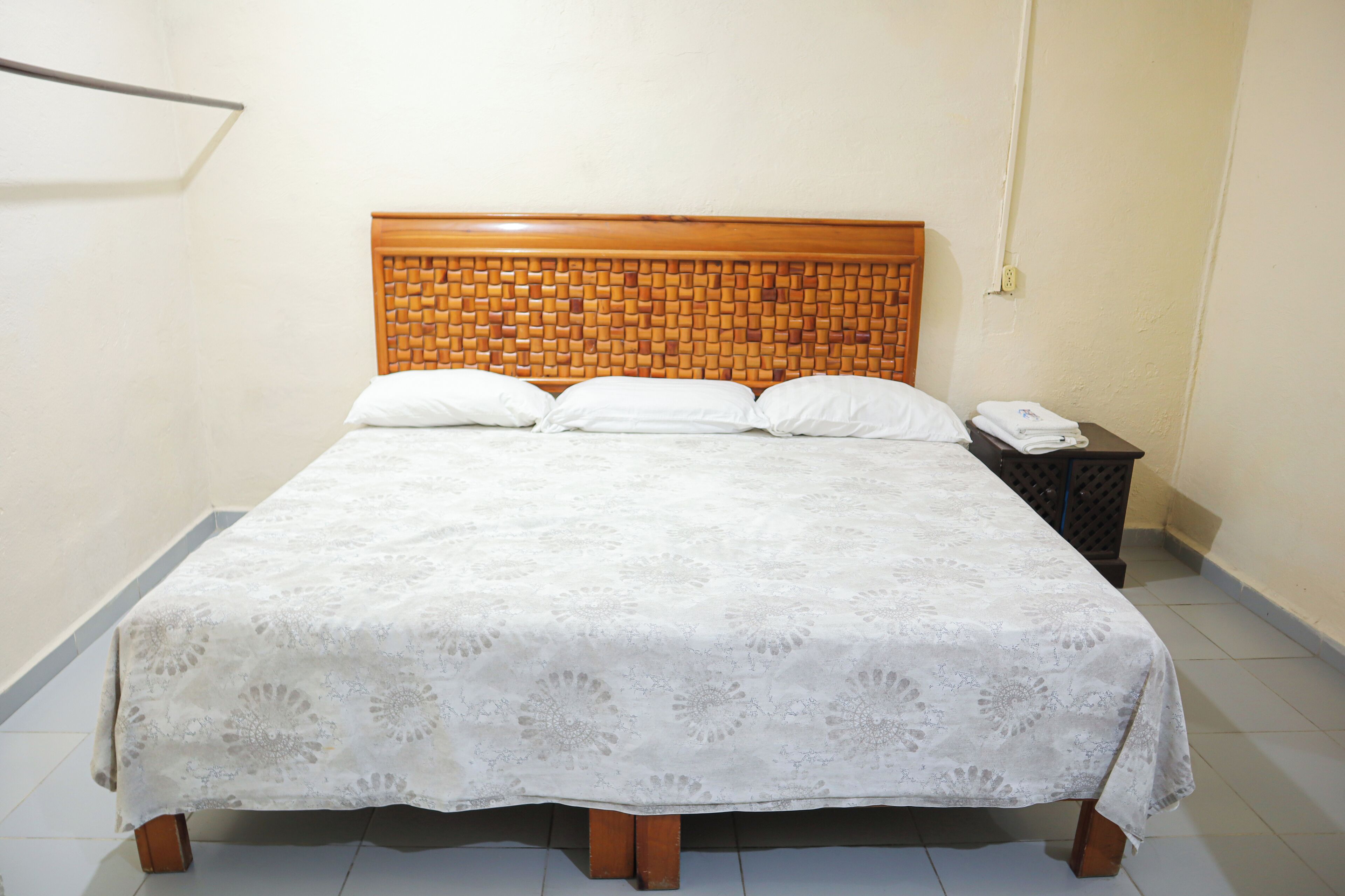 A bed with a wooden headboard, white bedding, and a nightstand with a phone.