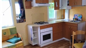 Ett kompakt kök med träskåp, en gasspis, en ugn och en matplats med ett bord och stolar.