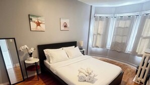 A bedroom with a bed, a bedside table, a mirror, and a window with curtains.