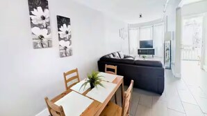 A modern living room with a dark sofa, a wooden dining table with chairs, and two floral wall art pieces.