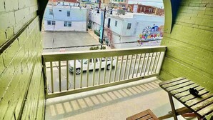 A balcony with a view of a cityscape, including a tall building and parked cars.
