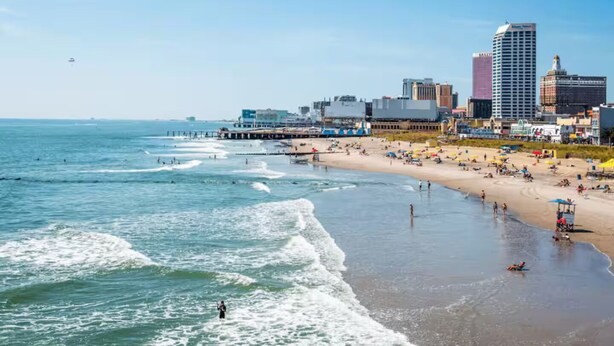 A beach with waves, a pier, and a city skyline in the background.
