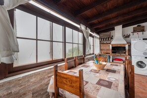 A dining area with a table, chairs, a large window, a brick wall, a fireplace, and a washing machine.