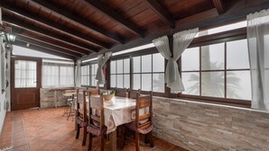 A dining area with a wooden ceiling, stone walls, and large windows with curtains.