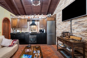 A kitchen with wooden cabinets, a stone wall, a large refrigerator, and a flat-screen TV mounted on the wall.