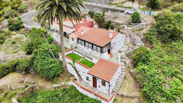 A white building with a red roof, surrounded by greenery and a palm tree.