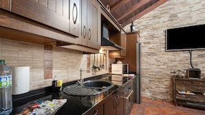 A kitchen with wooden cabinets, a stone wall, a black countertop, and a tiled floor.