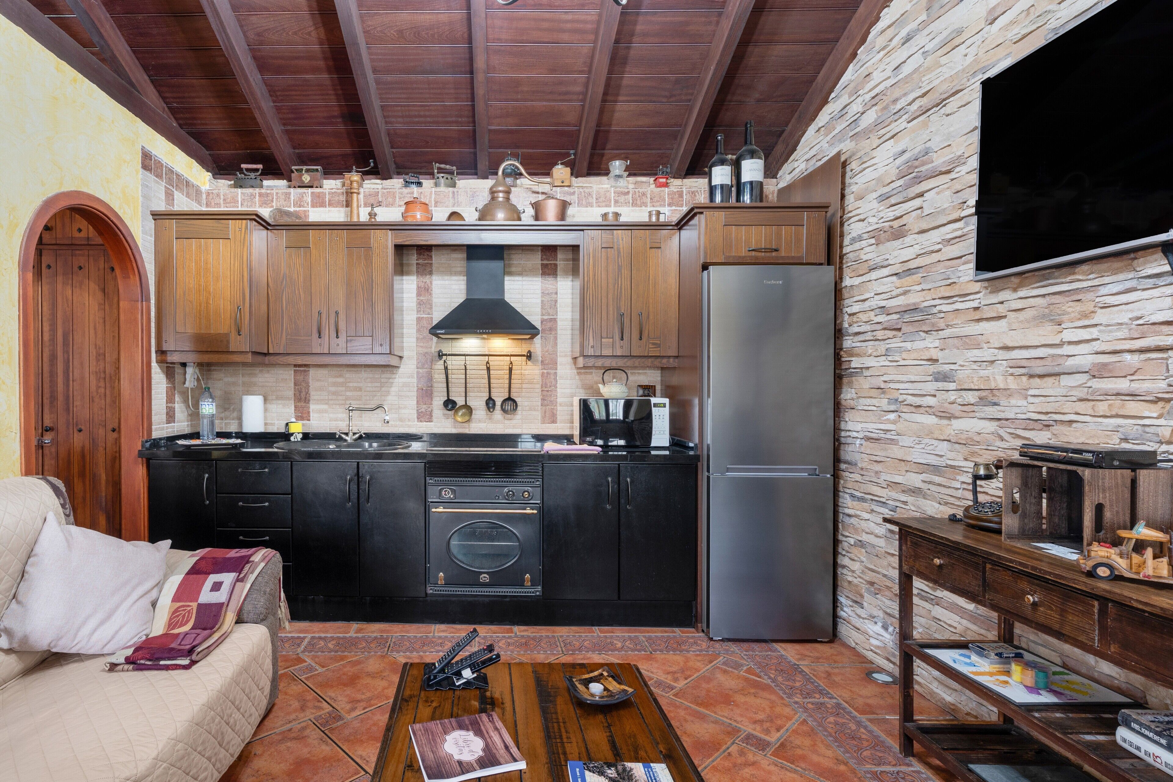 Una cocina con armarios de madera, pared de piedra, horno empotrado y refrigerador.