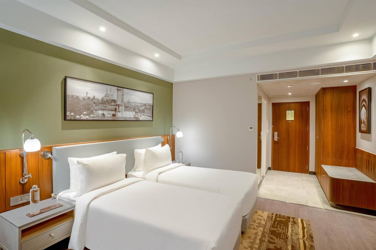 A hotel room with a double bed, bedside lamps, a nightstand, a framed picture on the wall, and a wooden wardrobe.