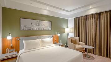 A hotel room with a large bed, a nightstand, a desk, a chair, a table, and a lamp.