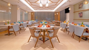 A modern dining area with round tables, grey upholstered chairs, and pendant lighting. - Park Inn By Radisson Lucknow Vikas Nagar (Lucknow)