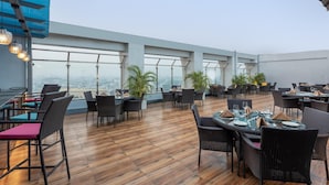 An outdoor dining area with wooden flooring, black wicker chairs, and tables set for dining. - Park Inn By Radisson Lucknow Vikas Nagar (Lucknow)