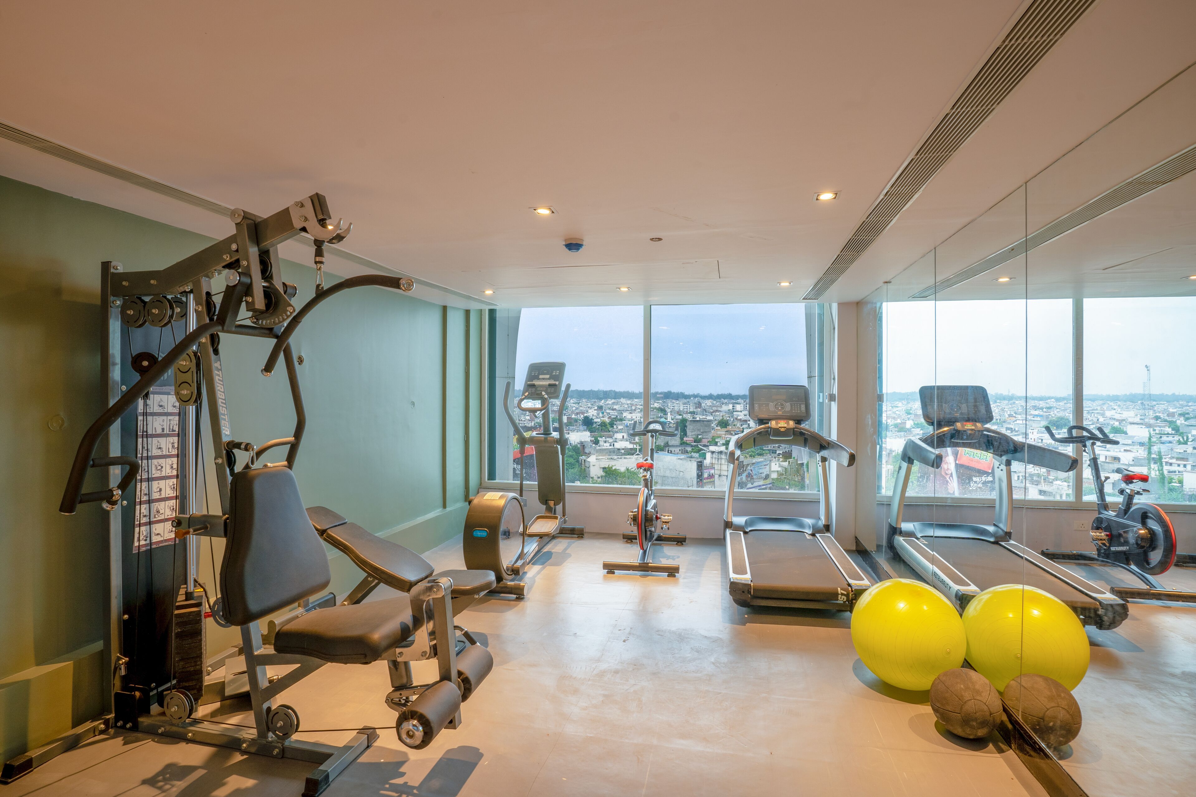 A gym with exercise equipment, treadmills, and large windows offering a city view.