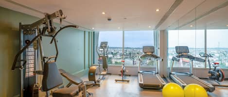 A gym with exercise equipment, treadmills, and large windows offering a city view.