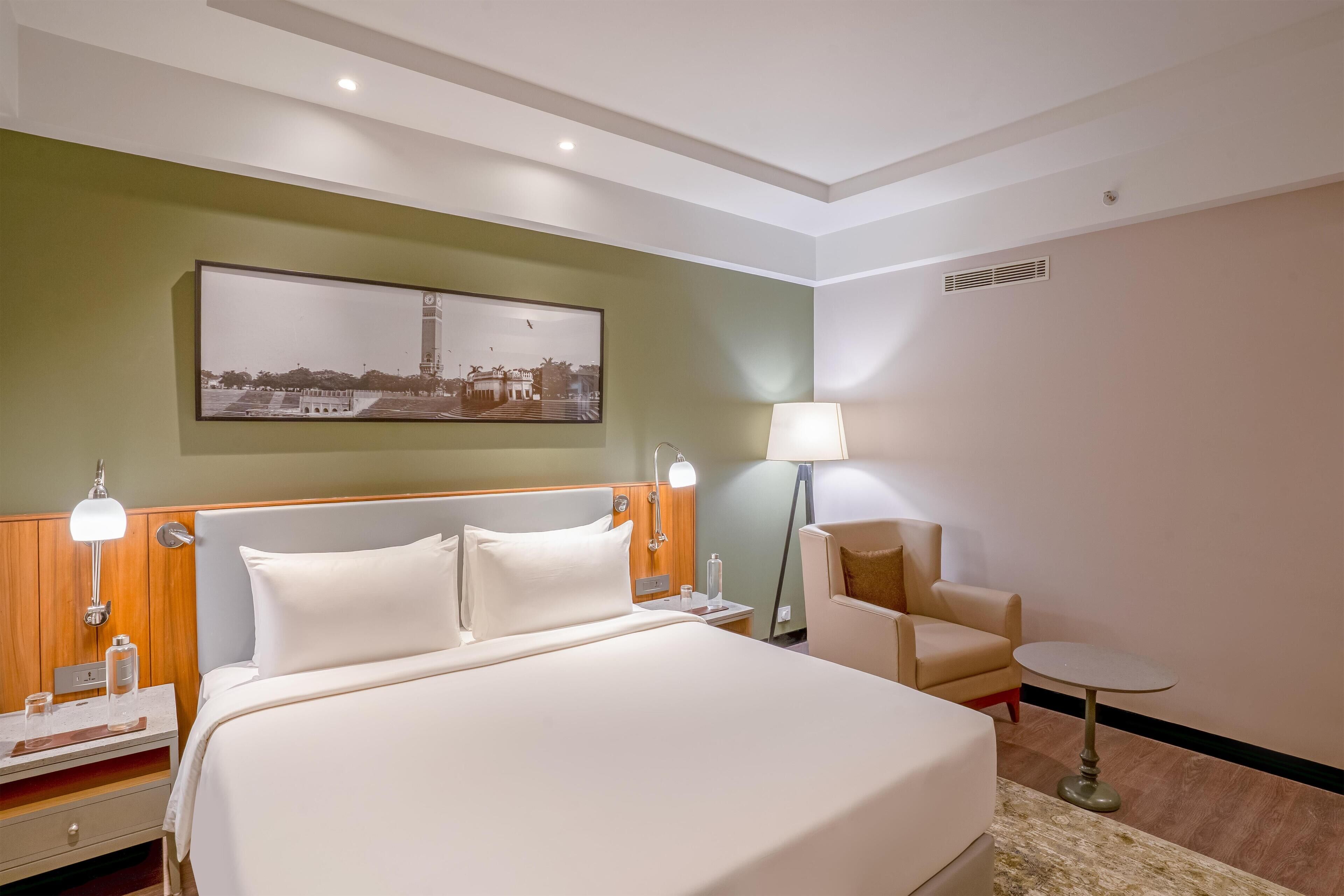 A hotel room with a large bed, bedside tables, a chair, a small table, and a picture on the wall.