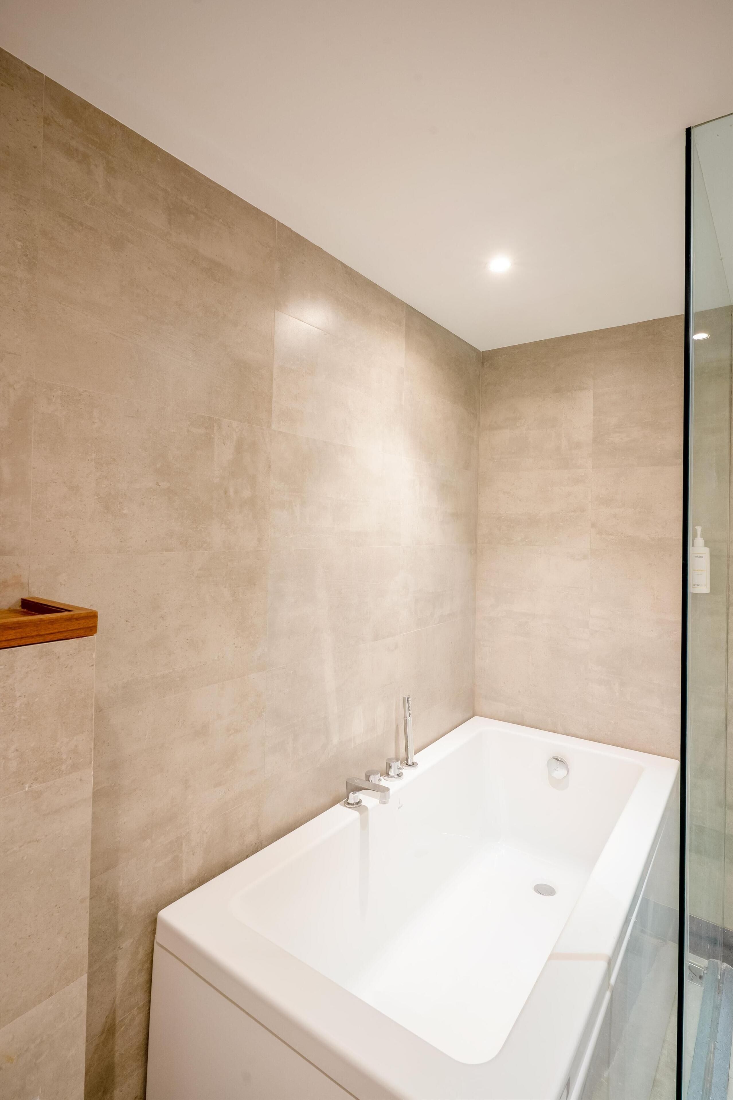 A modern bathroom with a large bathtub, a glass shower enclosure, and beige tiled walls.