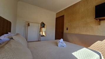 Habitación de hotel con cama, espejo, puerta y televisión montada en la pared.