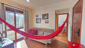 Quarto com rede, sofá e porta que dá acesso a outro espaço.