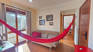 A room with a hammock, a sofa, and a door leading to another space. - Estadia Tri Ótima Localização e Garagem (Porto Alegre)