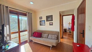 Sala de estar com sofá, televisão e varanda com vista.