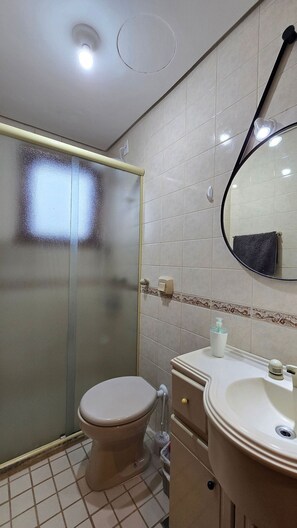 A bathroom with a toilet, sink, mirror, and glass shower enclosure. - Estadia Tri Ótima Localização e Garagem (Porto Alegre)