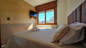 Un dormitorio con cama, ventana y televisor en la pared.