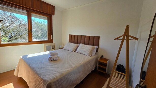 Un dormitorio con una cama, una ventana, un radiador y una silla de madera.