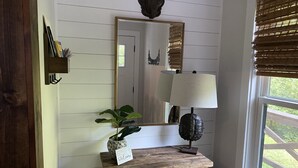 A rustic interior with a wooden console table, a potted plant, a mirror, and a lamp.