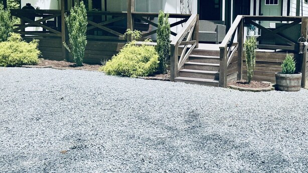 A rustic cabin with a porch, a staircase, and a gravel driveway.