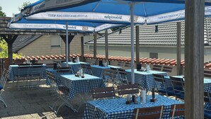 An outdoor seating area with blue checkered tables and umbrellas, featuring the logo 'Weihenstephan'. - Hotel Restaurant Ampertal (Haag an der Amper)