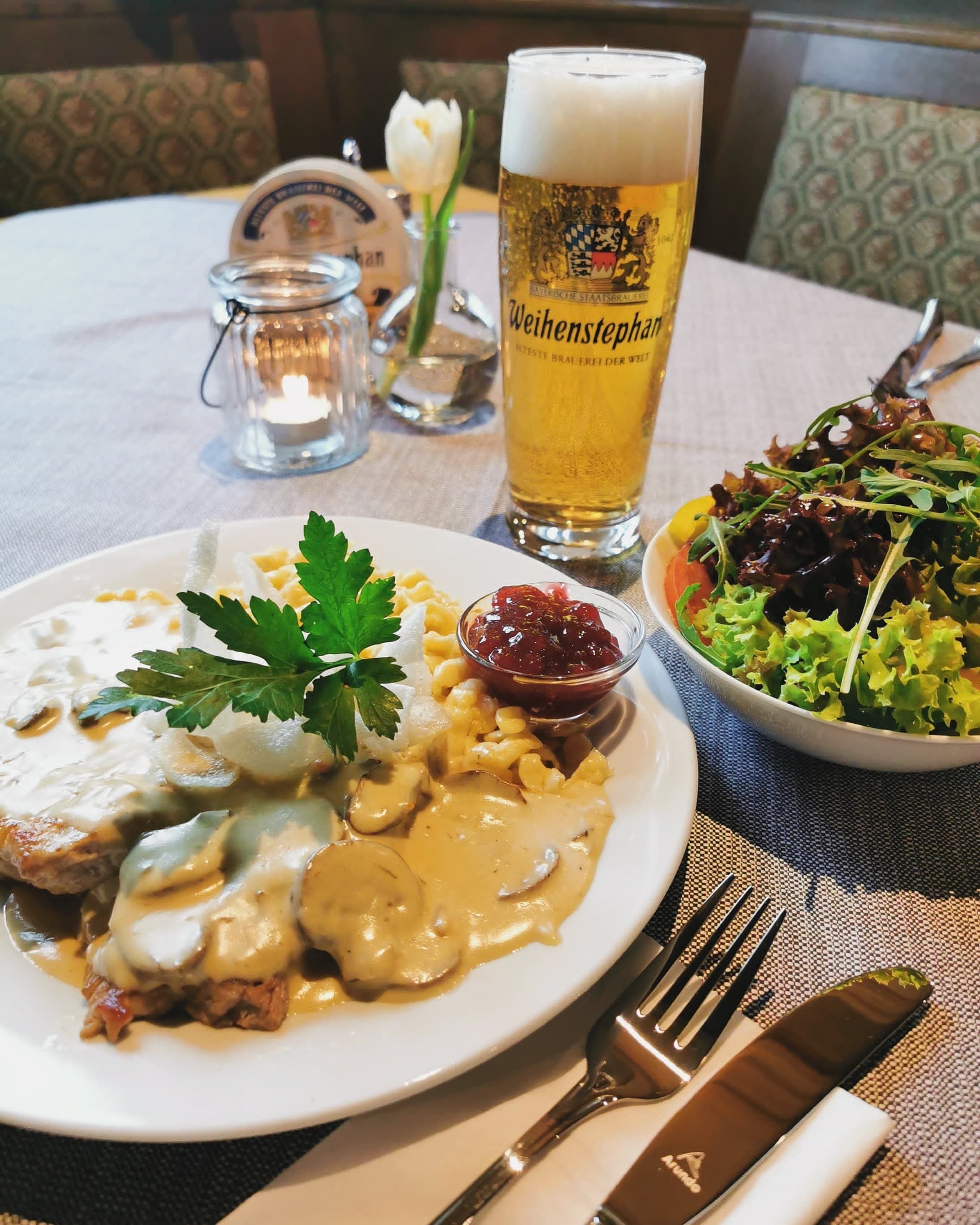 Ein Esstisch mit einer Speise, einem Bierglas und einer Salatschüssel.