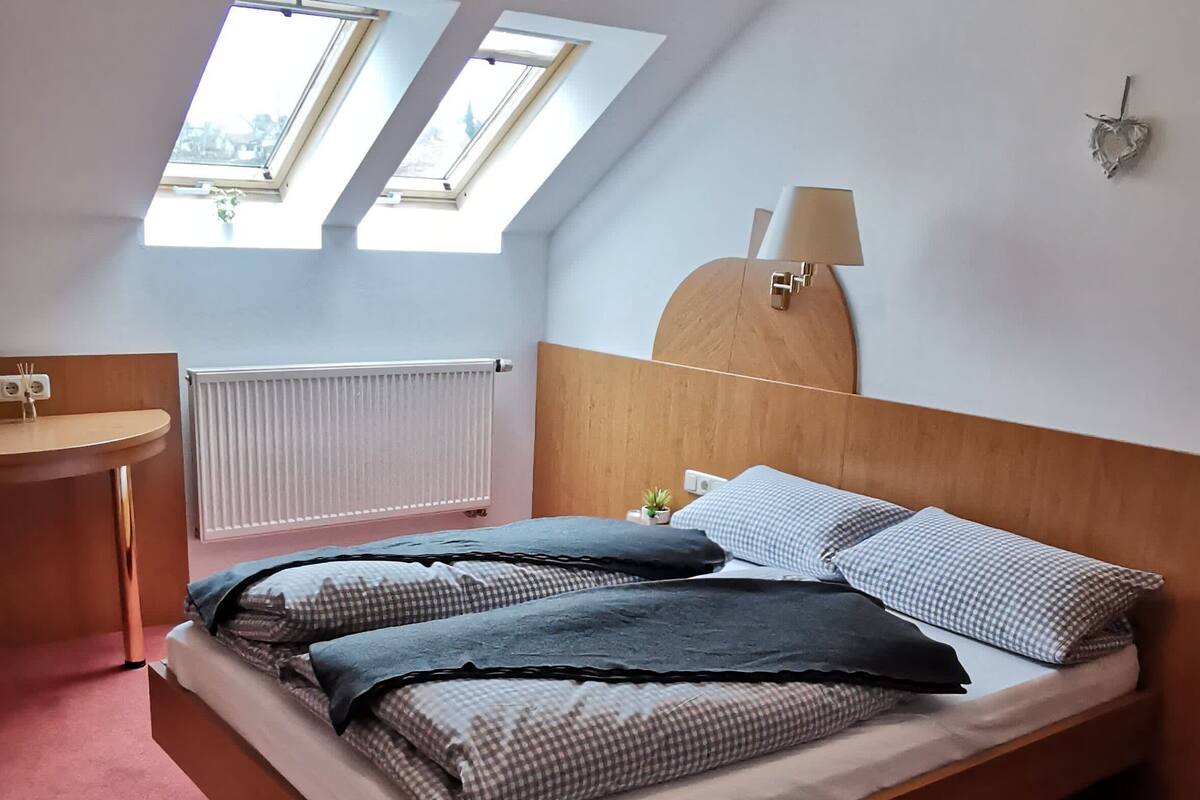 A bedroom with a wooden bed, a bedside table, a radiator, and a skylight.