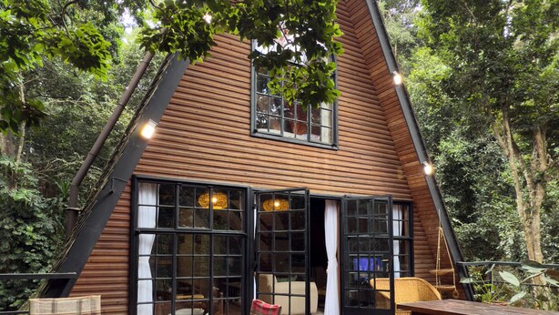 Una cabaña de madera con un amplio patio descubierto, amueblado con mesas y sillas de madera, rodeada de abundante vegetación.