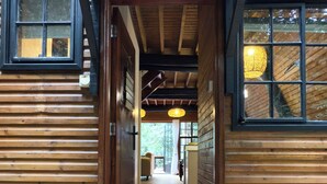 Entrada de una cabaña de madera con un felpudo, un pasillo que conduce a una habitación y una ventana con una lámpara colgante.