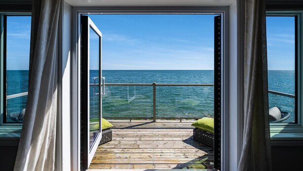 Une terrasse en bois avec une rambarde en verre donnant sur la mer.