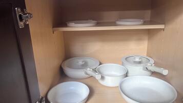 A kitchen cabinet with white ceramic cookware, including pots, pans, and bowls.