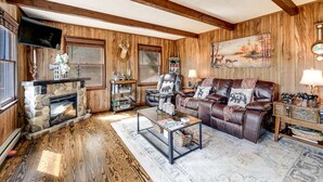 A cozy living room with a stone fireplace, leather sofa, and wooden walls. - Whisper Mountain Retreat (Franklin)