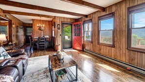 A cozy cabin interior with wooden walls, a dining area, a leather sofa, and large windows offering a view of the outdoors. - Whisper Mountain Retreat (Franklin)
