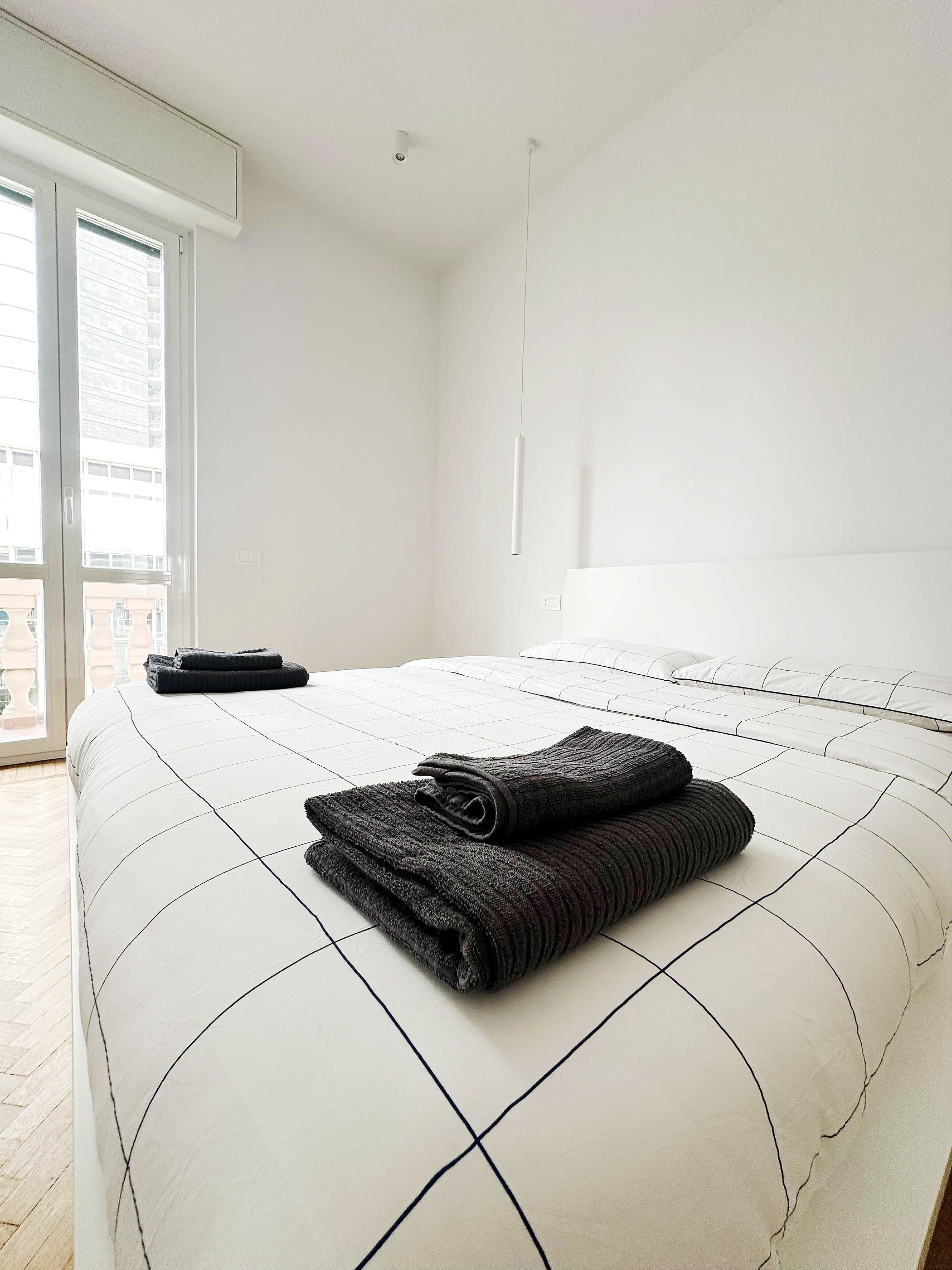 Habitación de hotel con una cama grande, una ventana con persianas y vistas a edificios.