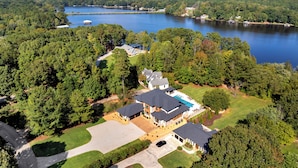 A large, two-story house with a swimming pool, surrounded by dense forest and a lake.