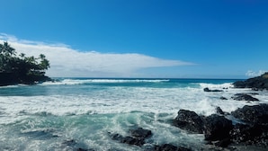 A beach with waves crashing onto dark rocks and a clear blue sky. - Kona Farm Stay - Amazing Ocean and Sunset Views (Kailua-Kona)