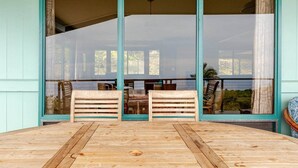 A wooden deck with two wooden benches facing a large sliding glass door leading to an outdoor area with a table and chairs. - Kona Farm Stay - Amazing Ocean and Sunset Views (Kailua-Kona)